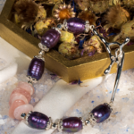 دستبند زنانه شوکا با سنگ رز کوارتز و مروارید بنفش، آویز صلیب نقره‌ای، طراحی دست‌ساز و خاص.