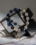 خرید دستبند زنانه شوکا با سنستیک آبی، مروارید سفید و آویز تاج نقرهای، طراحی شیک و دستساز.