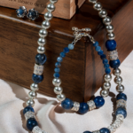 ست زیورآلات زنانه شوکا شامل گردنبند، دستبند و گوشواره با سنگ سودالیت طبیعی و مروارید نقره‌ای. طراحی لوکس با ترکیب رنگ آبی و سرمه‌ای مناسب استایل‌های شیک.