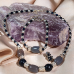 ست زیورآلات زنانه شوکا شامل گردنبند، دستبند و گوشواره با سنگ عقیق طبیعی، گلدستون و مروارید. ترکیب رنگ طوسی و سرمه‌ای با طراحی لوکس و دست‌ساز.