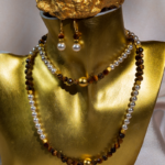 ست زیورآلات زنانه شوکا با ترکیب سنگ طبیعی چشم ببر قهوه‌ای و مروارید سفید. شامل گردنبند، دستبند و گوشواره با طراحی کلاسیک و جزئیات طلایی.